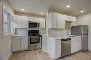 Kitchen featuring stainless steel appliances, white cabinets, light wood-type flooring, recessed lighting, and light stone countertops