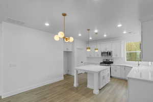 Kitchen featuring white cabinetry, a kitchen island, light wood-style flooring, pendant lighting, and stainless steel microwave