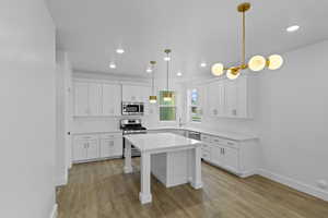 Kitchen featuring appliances with stainless steel finishes, white cabinets, light wood-type flooring, decorative light fixtures, and recessed lighting