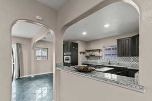 Kitchen featuring light stone counters, tasteful backsplash, arched walkways, plenty of natural light, and a textured wall