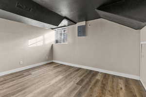 Additional living space featuring a textured wall, electric panel, wood finished floors, a textured ceiling, and lofted ceiling