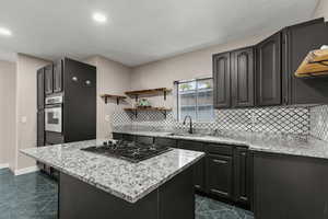 Kitchen with light stone counters, a center island, backsplash, open shelves, and black gas cooktop