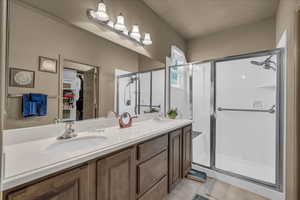 Full bath featuring double vanity, light tile patterned floors, a shower stall, and a walk in closet