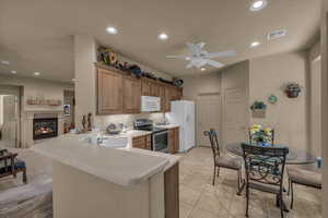 Kitchen with white appliances, recessed lighting, a peninsula, light countertops, and brown cabinets