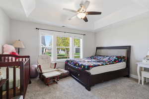 Carpeted bedroom featuring a raised ceiling, a ceiling fan, and a crib