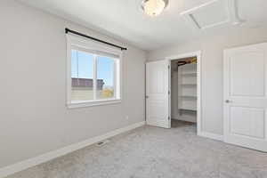Unfurnished bedroom with a walk in closet, light colored carpet, and attic access