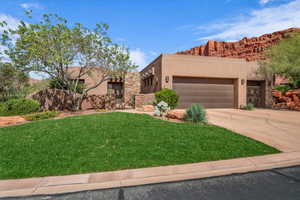 Pueblo revival-style home featuring stucco siding, a front yard, driveway, an attached garage, and a mountain view