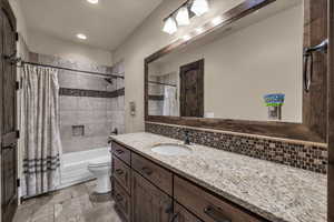 Full bath with vanity, shower / bath combo with shower curtain, decorative backsplash, stone tile floors, and recessed lighting