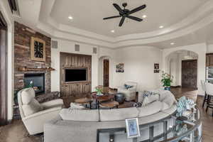 Living area with a tray ceiling, recessed lighting, a fireplace, arched walkways, and ceiling fan