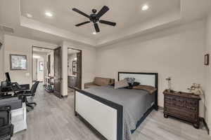 Bedroom featuring a raised ceiling, light wood finished floors, ensuite bath, and recessed lighting