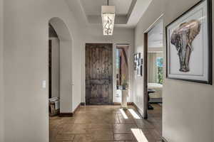 Entrance foyer with stone tile floors, arched walkways, and a raised ceiling