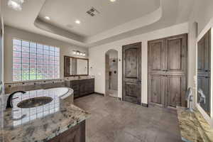 Full bathroom featuring a tray ceiling, vanity, walk in shower, stone tile floors, and recessed lighting