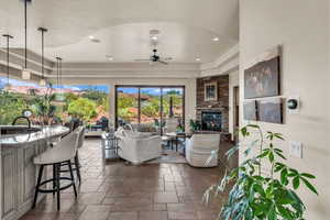 Living area featuring stone tile floors, ceiling fan, recessed lighting, a stone fireplace, and a raised ceiling