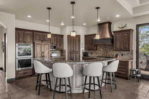 Kitchen with hanging light fixtures, appliances with stainless steel finishes, a breakfast bar, a large island with sink, and recessed lighting