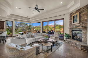 Living area featuring a tray ceiling, recessed lighting, a ceiling fan, stone tile flooring, and a stone fireplace