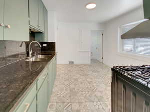 Kitchen with green cabinets, tasteful backsplash, dark stone countertops, wall chimney range hood, and black range with gas cooktop