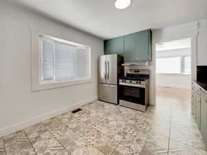 Kitchen with green cabinets, appliances with stainless steel finishes, light tile patterned flooring, and under cabinet range hood