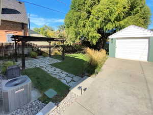 Fenced backyard featuring a pergola, a patio area, driveway, an outbuilding, and a garage