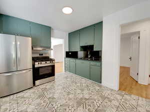 Kitchen with appliances with stainless steel finishes, green cabinetry, tasteful backsplash, under cabinet range hood, and dark stone counters