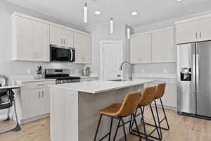Kitchen with appliances with stainless steel finishes, a kitchen island with sink, a kitchen bar, light wood-style floors, and pendant lighting