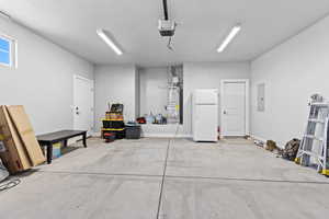 Garage featuring freestanding refrigerator, strapped water heater, a garage door opener, and electric panel