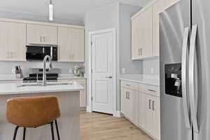 Kitchen featuring appliances with stainless steel finishes, light wood finished floors, light brown cabinetry, pendant lighting, and light stone counters