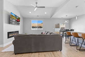 Living area with light wood-type flooring, a glass covered fireplace, a ceiling fan, and recessed lighting