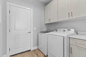 Laundry room with light wood-style floors, cabinet space, and washer and dryer