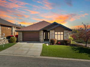 View of front of house with stone siding, a yard, driveway, and an attached garage