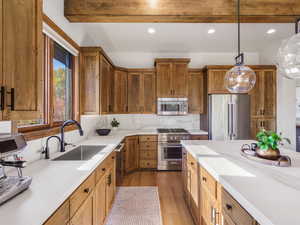 Kitchen with brown cabinets, premium appliances, light wood-style floors, decorative light fixtures, and backsplash