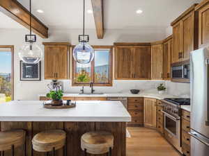 Kitchen with beam ceiling, a kitchen breakfast bar, brown cabinets, high quality appliances, and decorative light fixtures