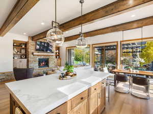 Kitchen with light wood-type flooring, beam ceiling, hanging light fixtures, recessed lighting, and a stone fireplace