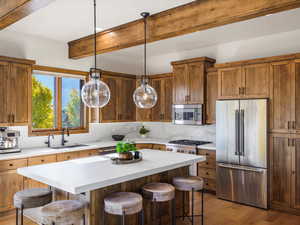 Kitchen with a kitchen bar, appliances with stainless steel finishes, hanging light fixtures, light wood-style floors, and a center island