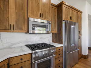 Kitchen featuring high quality appliances, brown cabinets, light stone countertops, and light wood-style floors