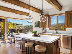 Kitchen with decorative light fixtures, beamed ceiling, light wood-style flooring, stainless steel dishwasher, and light countertops