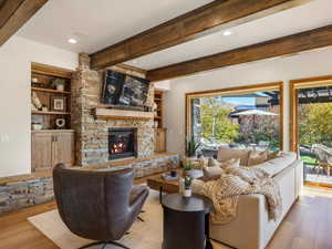 Living room featuring wood finished floors, beamed ceiling, a stone fireplace, recessed lighting, and built in features