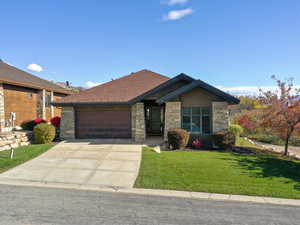 View of front of house with stone siding, a front lawn, driveway, and a garage