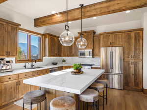 Kitchen featuring a kitchen bar, a kitchen island, light wood finished floors, brown cabinetry, and beamed ceiling