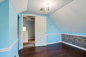 Bonus room with a textured ceiling, dark wood finished floors, vaulted ceiling, and a chandelier
