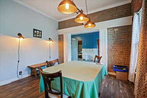 Dining room with brick wall, ornamental molding, and dark wood-type flooring