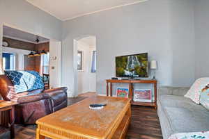 Living room featuring dark wood-style flooring, arched walkways, and ornamental molding