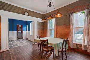 Dining room with brick wall, dark wood-type flooring, ornamental molding, washer / clothes dryer, and a wainscoted wall