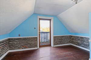 Additional living space with a textured ceiling, dark wood-style flooring, lofted ceiling, and wainscoting