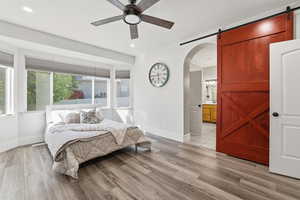 Bedroom with light wood finished floors, a barn door, a ceiling fan, arched walkways, and recessed lighting