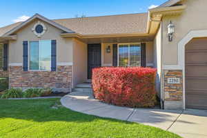 Doorway to property featuring stucco siding, roof with shingles, a lawn, covered porch, and stone siding