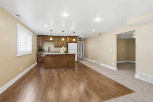 Kitchen featuring a center island, open floor plan, hanging light fixtures, brown cabinets, and freestanding refrigerator
