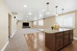 Kitchen featuring light stone counters, open floor plan, decorative light fixtures, a kitchen island, and dark colored carpet