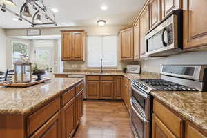 Kitchen with stainless steel appliances, light wood finished floors, brown cabinets, light stone counters, and recessed lighting