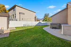 Fenced backyard with a trampoline, a patio, a mountain view, a shed, and a hot tub