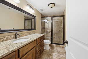 Full bathroom with vanity, a stall shower, and stone tile floors